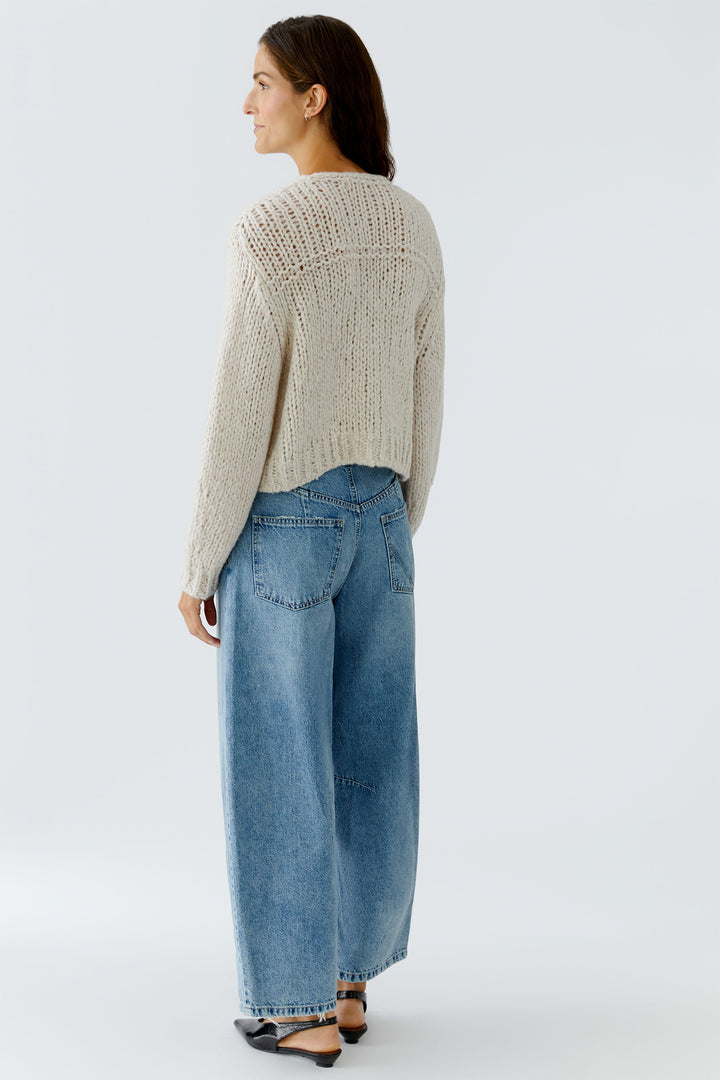 Woman wearing a beige knitted sweater and blue jeans on a white background