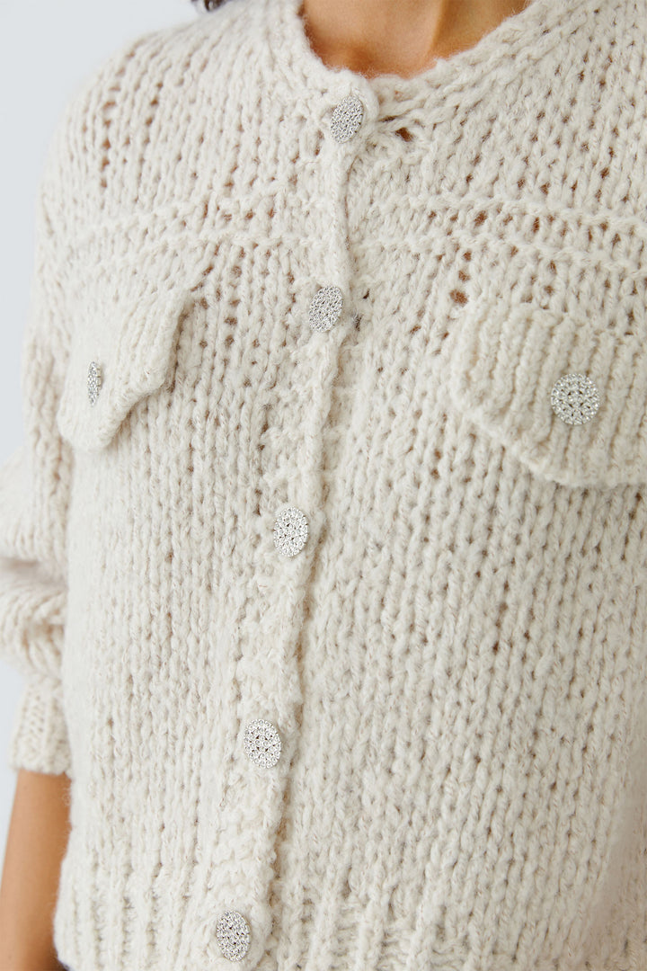 Close-up of a beige knitted cardigan with buttons on a plain background