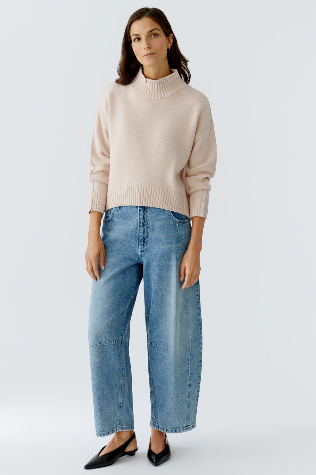 Woman wearing a beige sweater and blue jeans on a white background