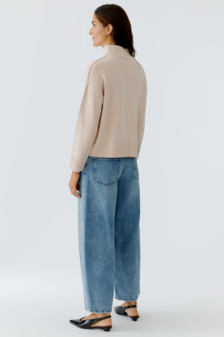 Woman wearing a beige sweater and blue jeans on a white background