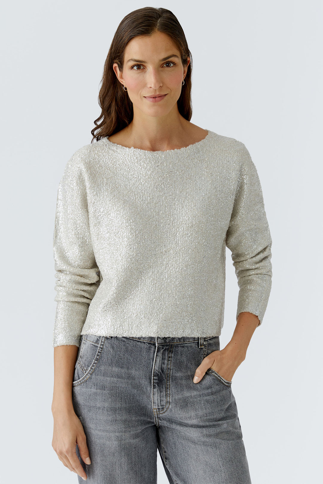Woman wearing a light gray sweater and gray jeans against a white background