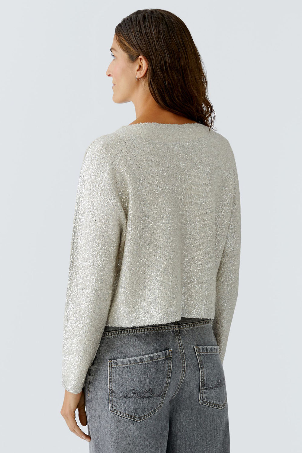 Woman wearing a light gray sweater and dark gray jeans on a light gray background