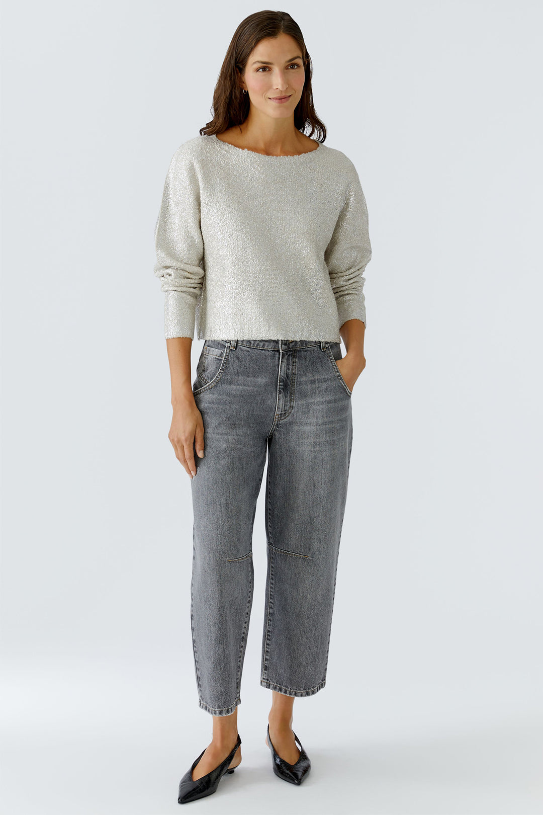 Woman wearing a light gray sweater and dark gray jeans on a white background