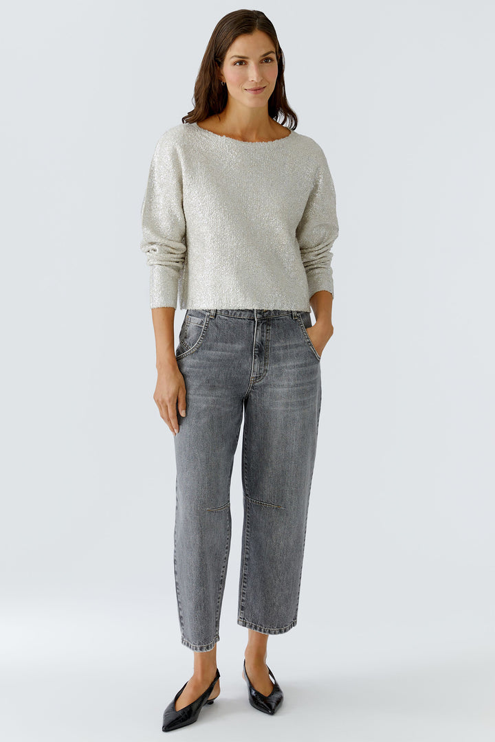 Woman wearing a light gray sweater and dark gray jeans on a white background