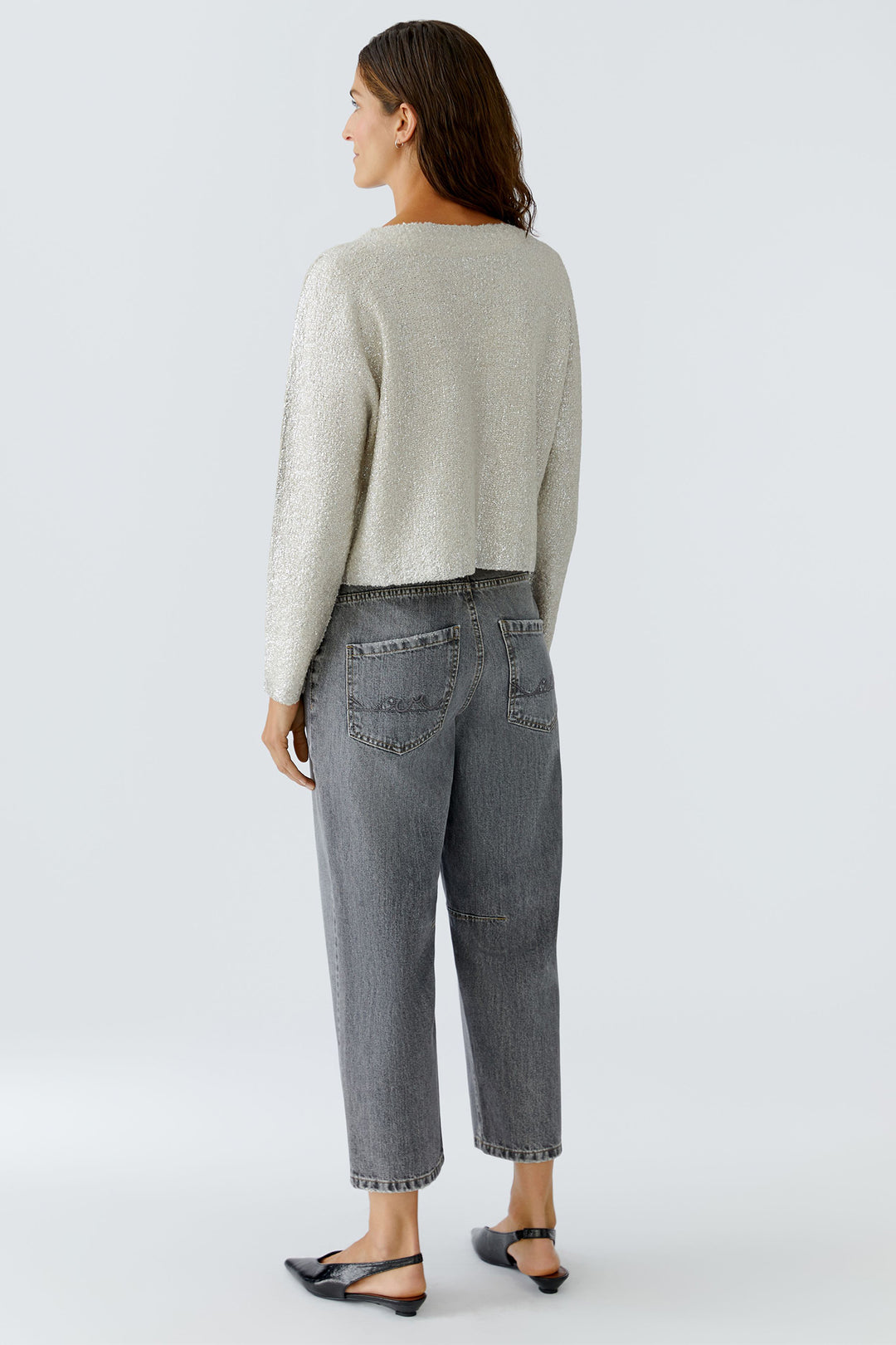 Woman wearing a light gray sweater and dark gray jeans on a white background