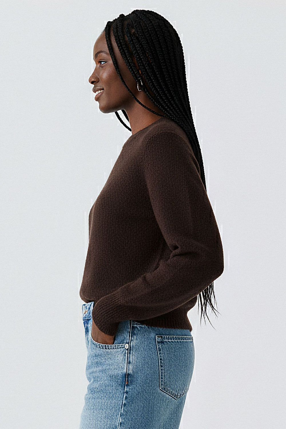 Woman wearing a brown sweater and blue jeans against a white background