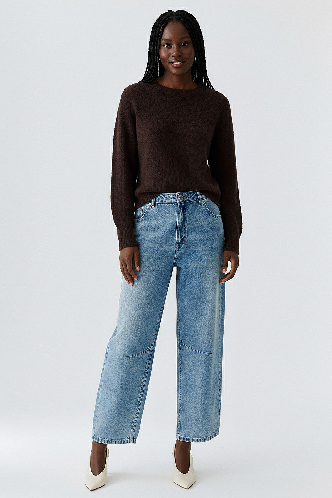Woman wearing a brown sweater and blue jeans on a white background