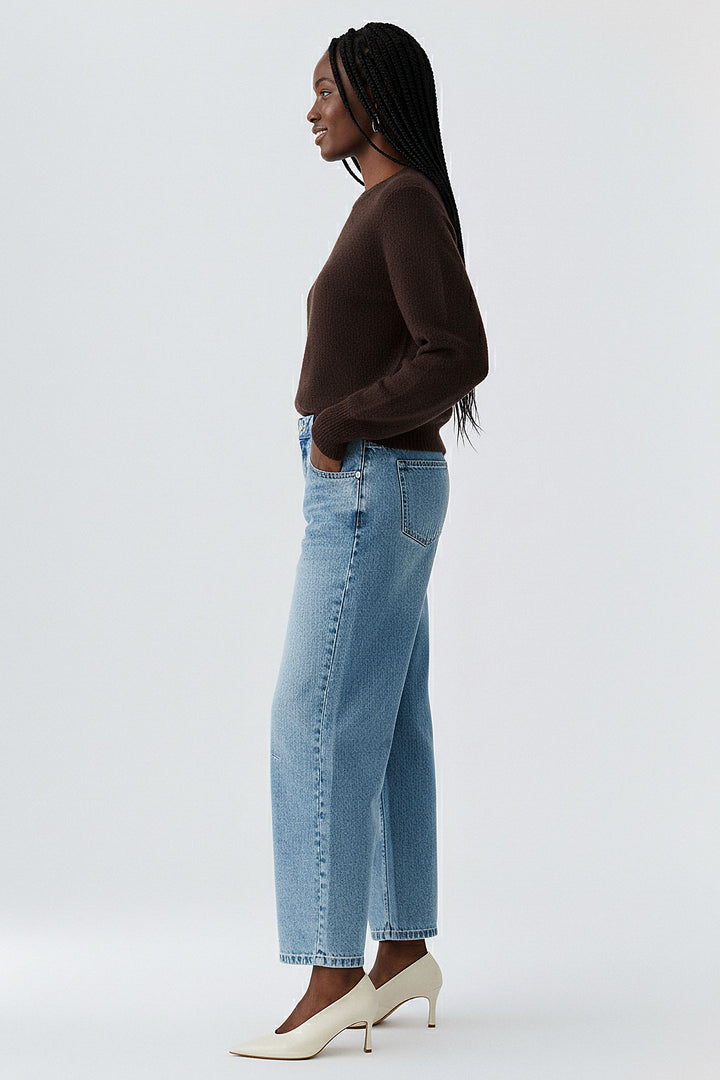 Woman wearing a brown sweater and light blue jeans on a white background
