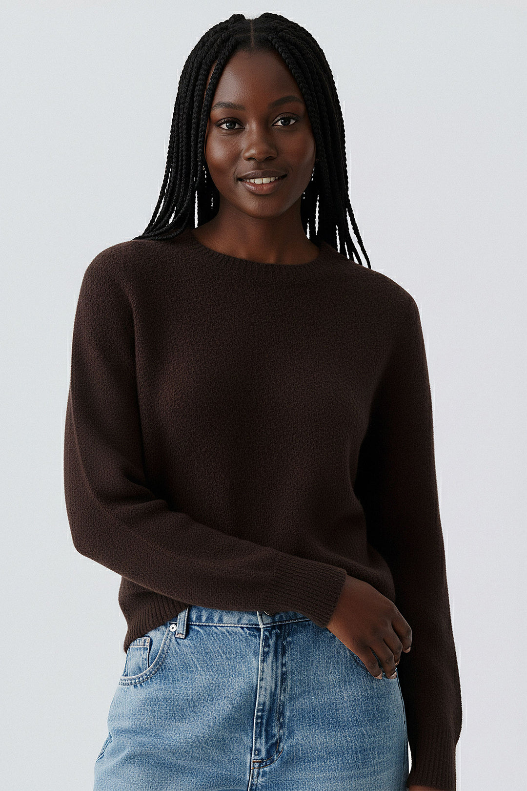 Woman wearing a brown sweater and blue jeans against a white background