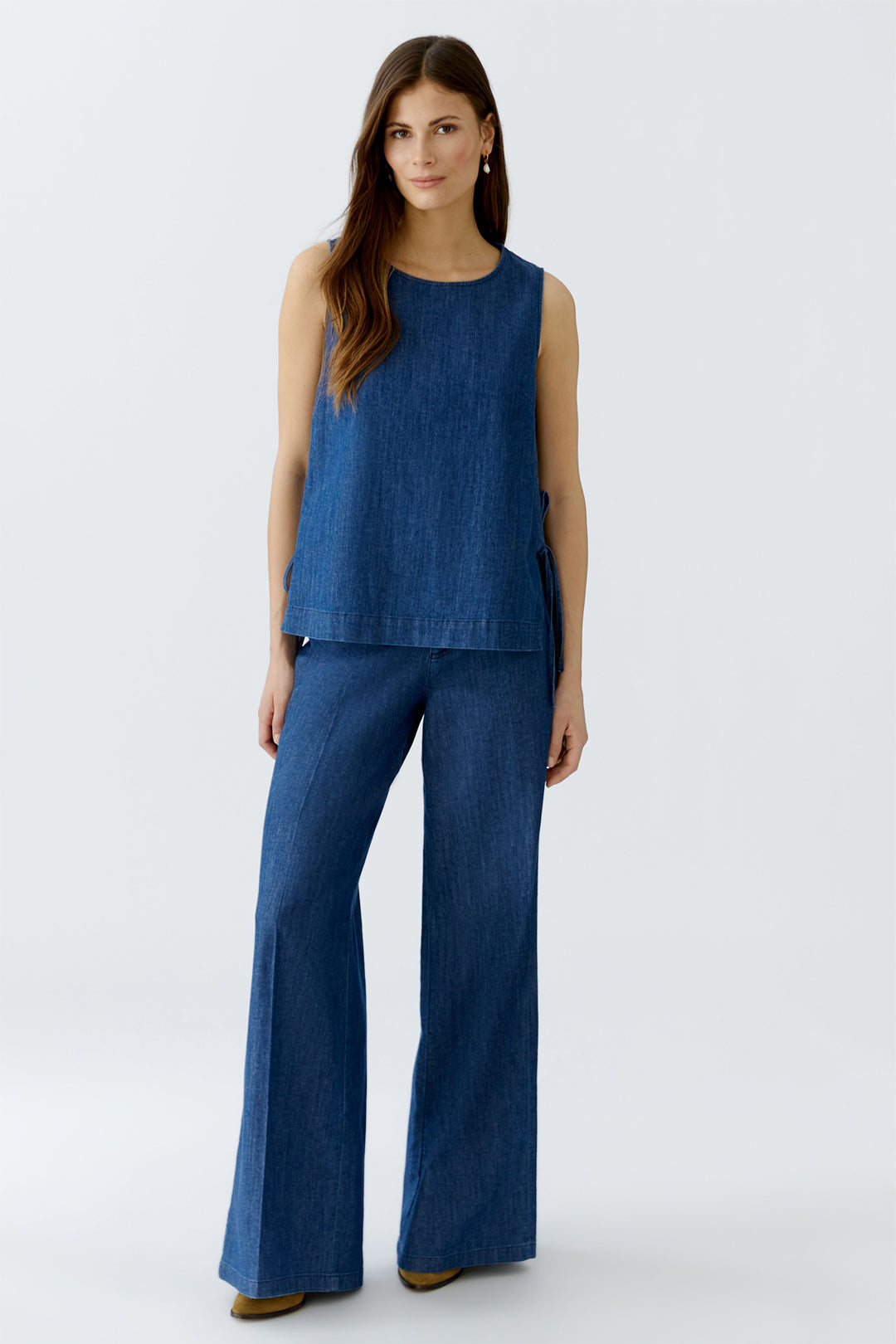 Woman wearing a blue sleeveless top and wide-leg pants on a white background