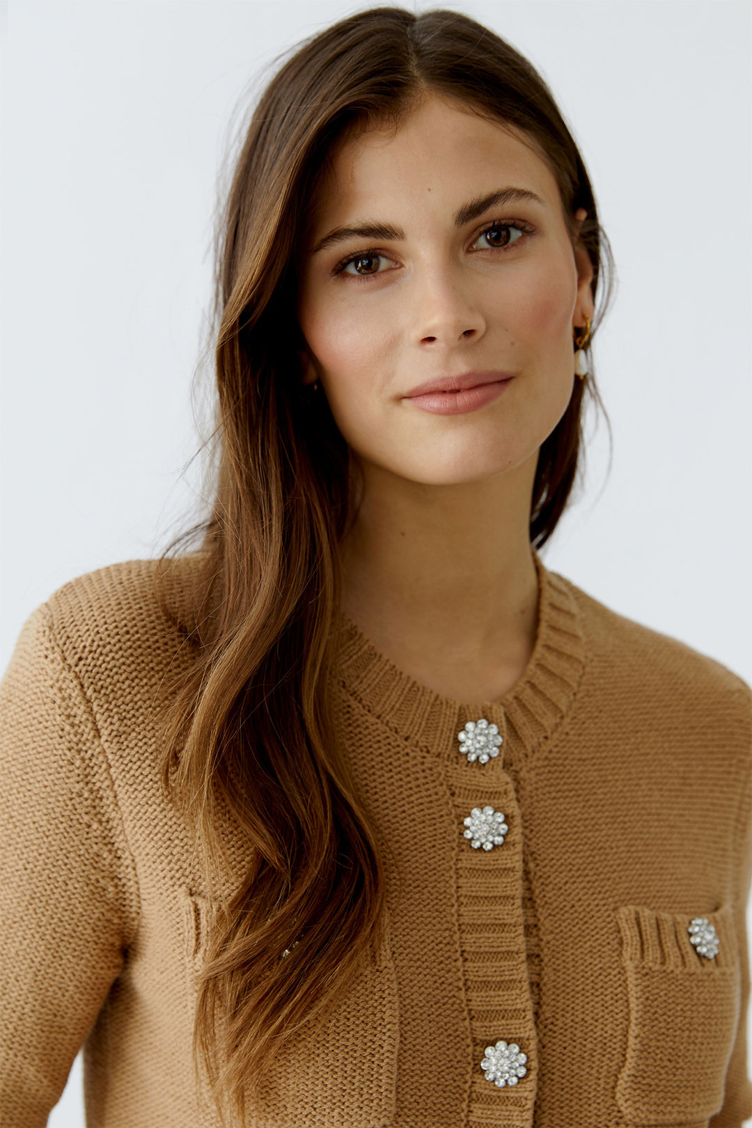 Woman wearing a brown knitted cardigan with decorative buttons on a white background