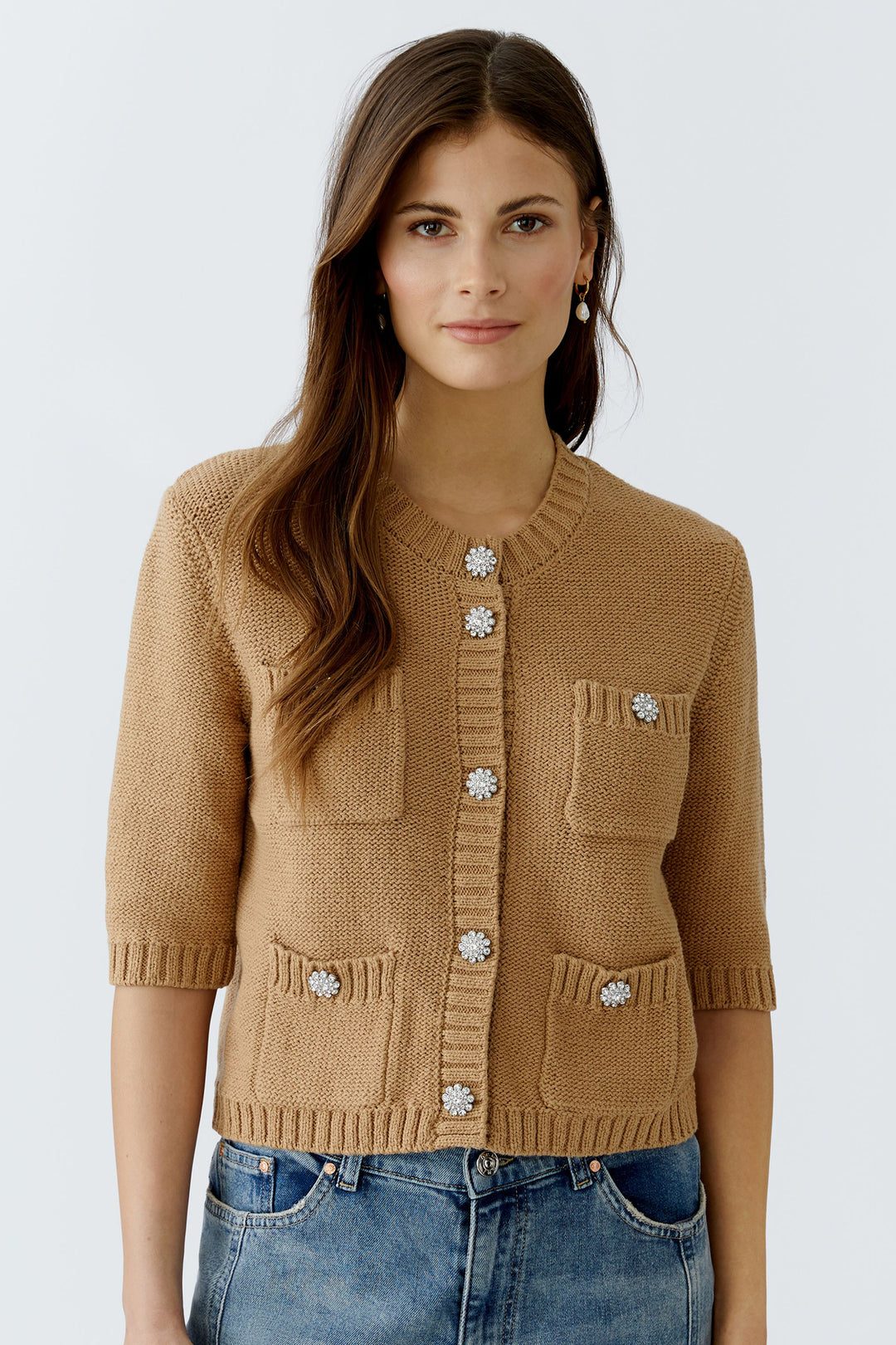 Woman wearing a brown knitted cardigan with decorative buttons on a white background