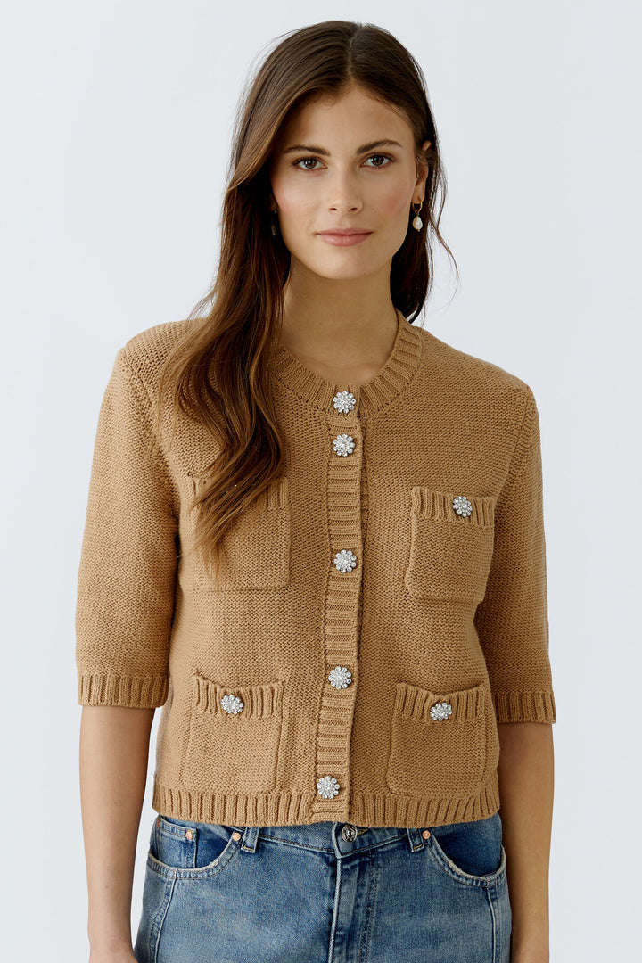 Woman wearing a brown knitted cardigan with decorative buttons on a white background