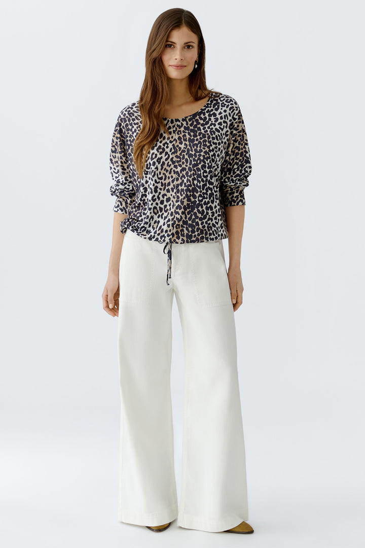 Woman wearing a patterned top and white pants on a white background