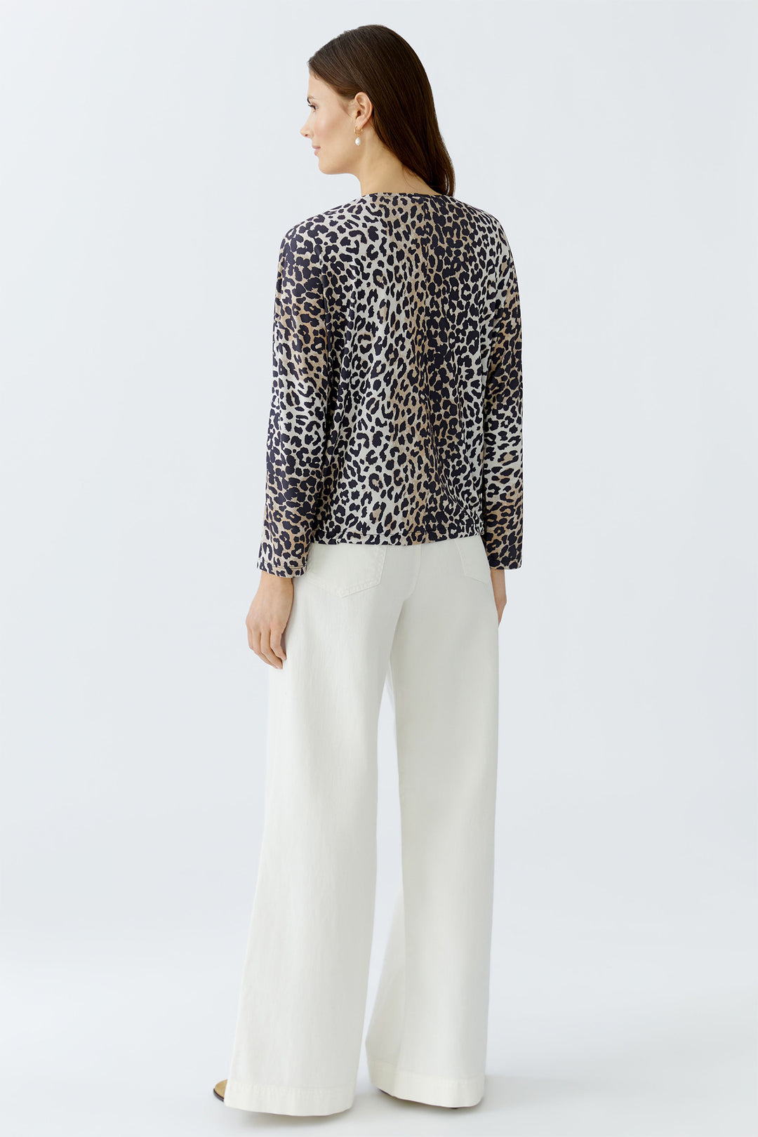 Woman wearing a leopard print top and white pants on a light gray background