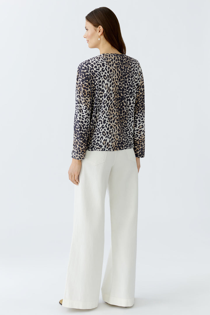 Woman wearing a leopard print top and white pants on a light gray background