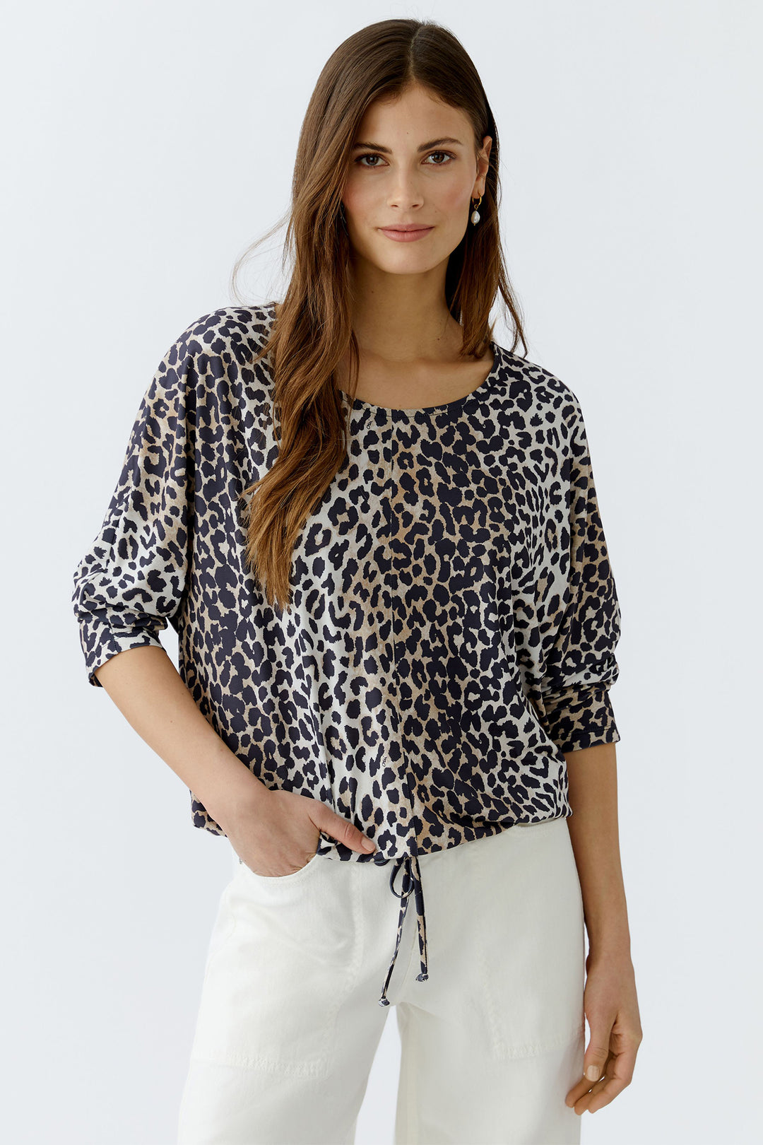 Woman wearing a leopard print top and white pants on a plain background