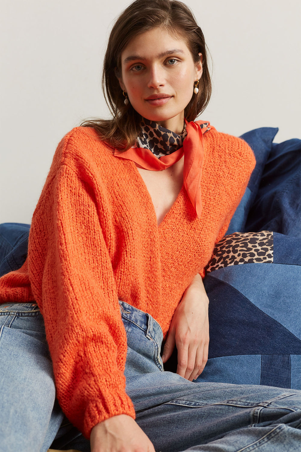 Woman wearing an orange sweater and blue jeans sitting on a blue couch.