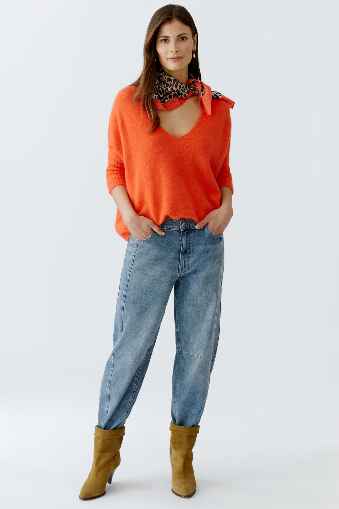 Woman wearing an orange sweater, blue jeans, and brown boots on a white background