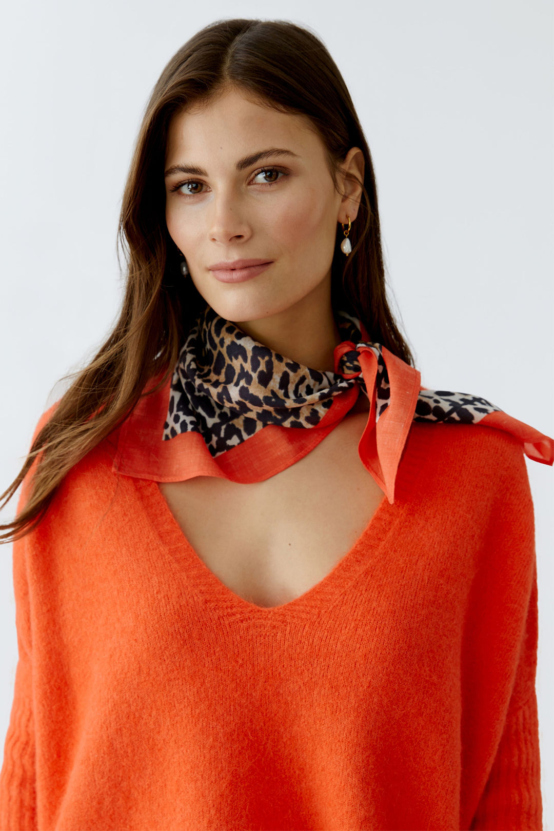 Woman wearing an orange sweater with a patterned scarf around her neck on a white background