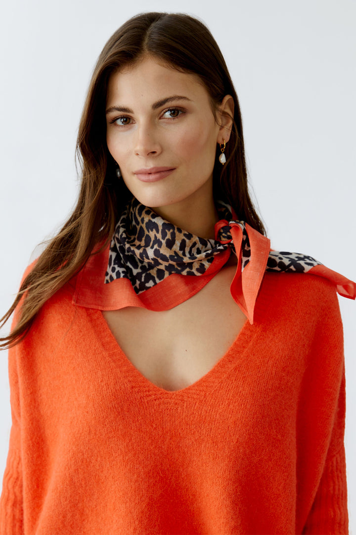 Woman wearing an orange sweater with a patterned scarf around her neck on a white background