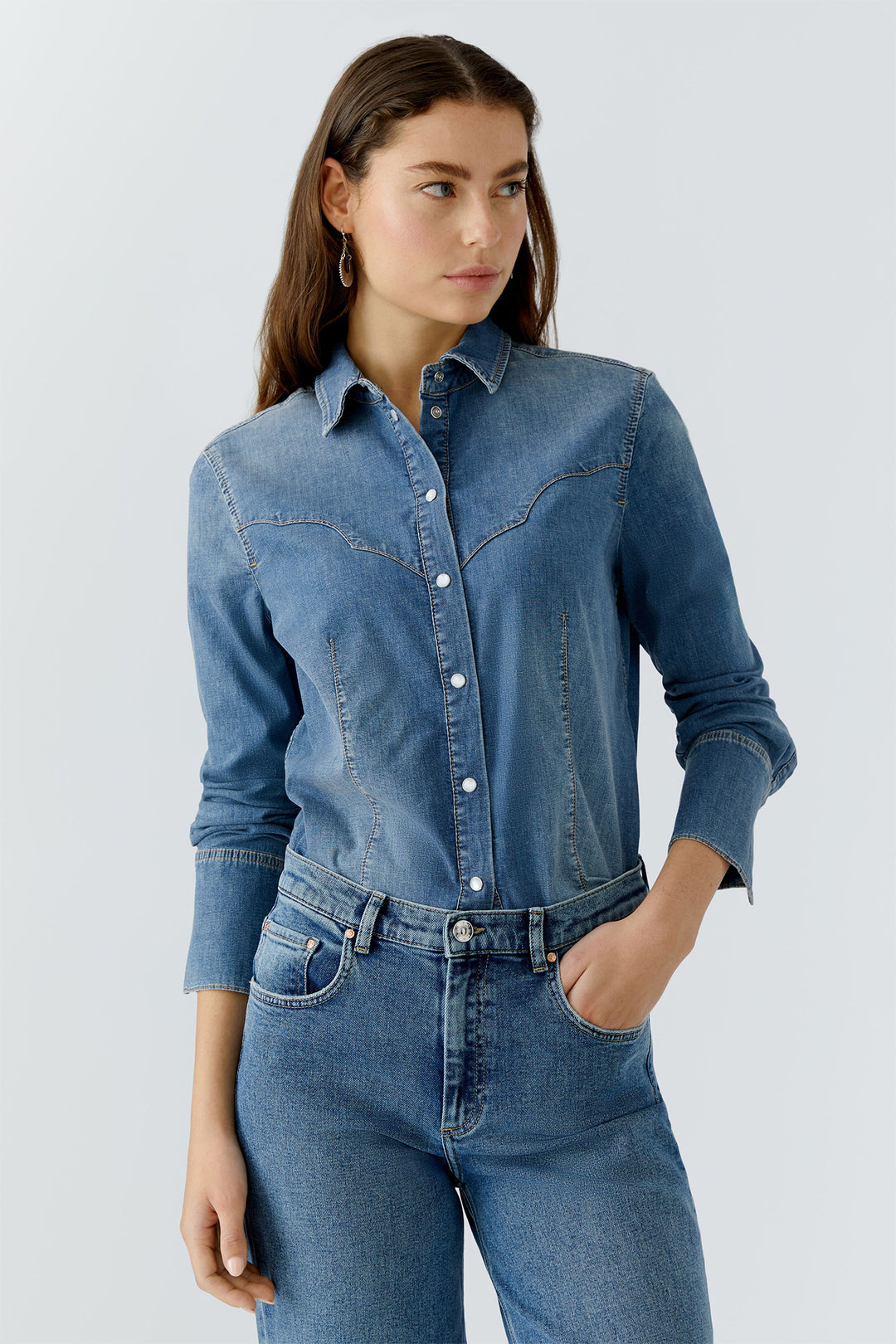 Woman wearing a blue denim shirt and jeans on a light gray background