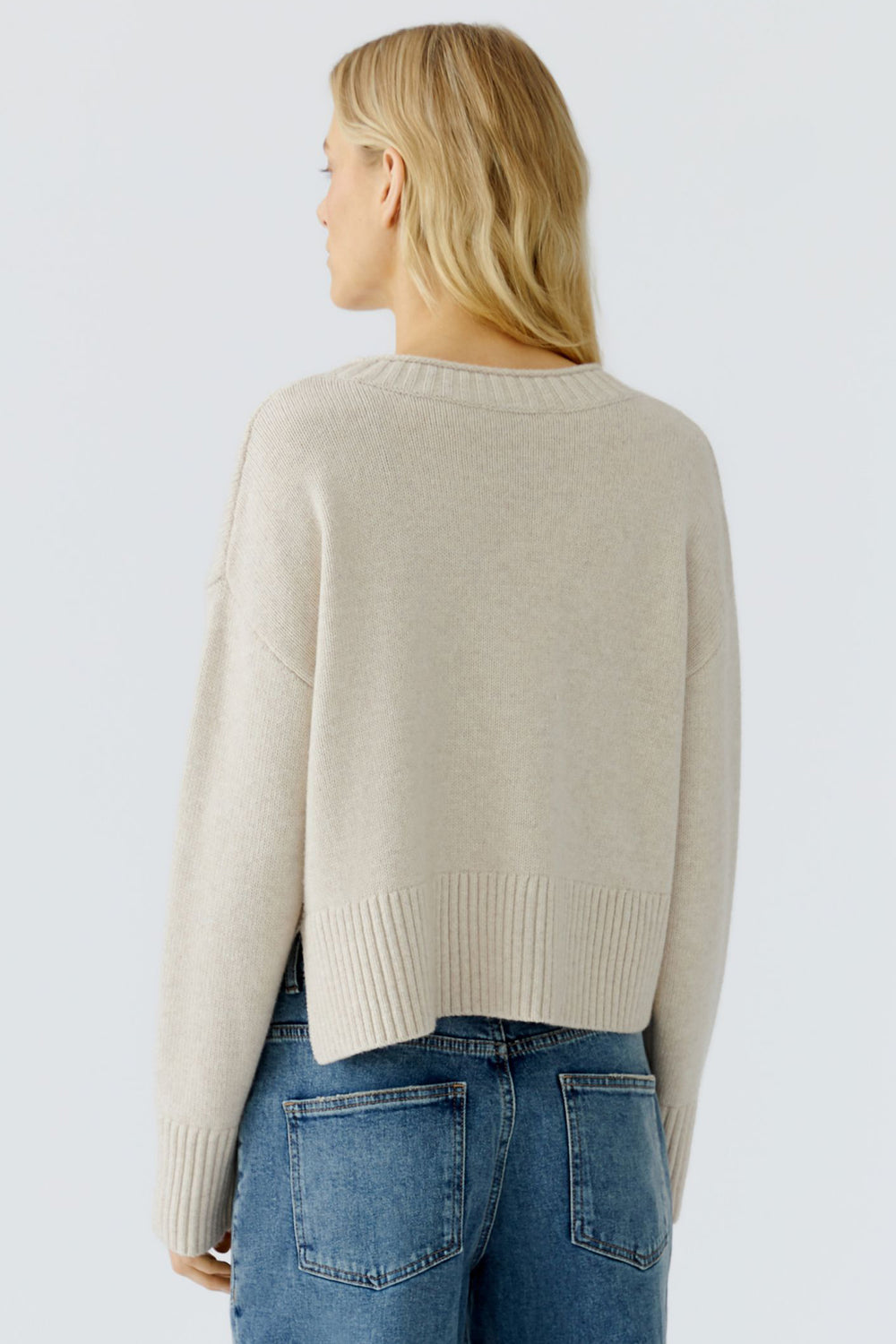 Woman wearing a beige sweater and blue jeans on a light gray background