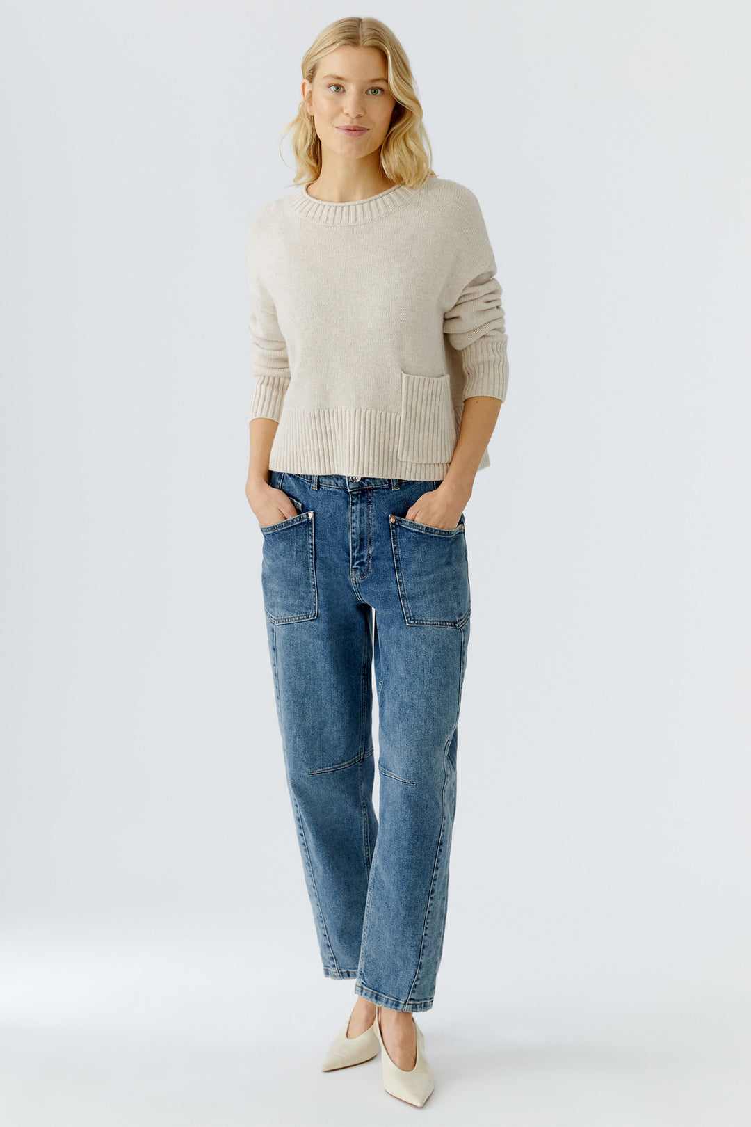 Woman wearing a beige sweater and blue jeans on a white background
