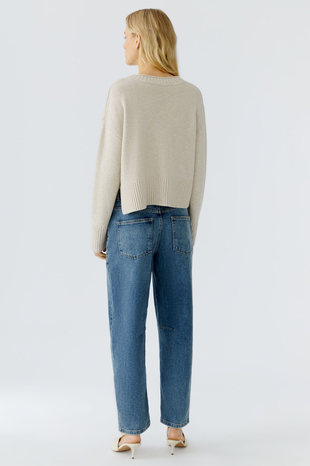 Woman wearing a beige sweater and blue jeans on a light gray background