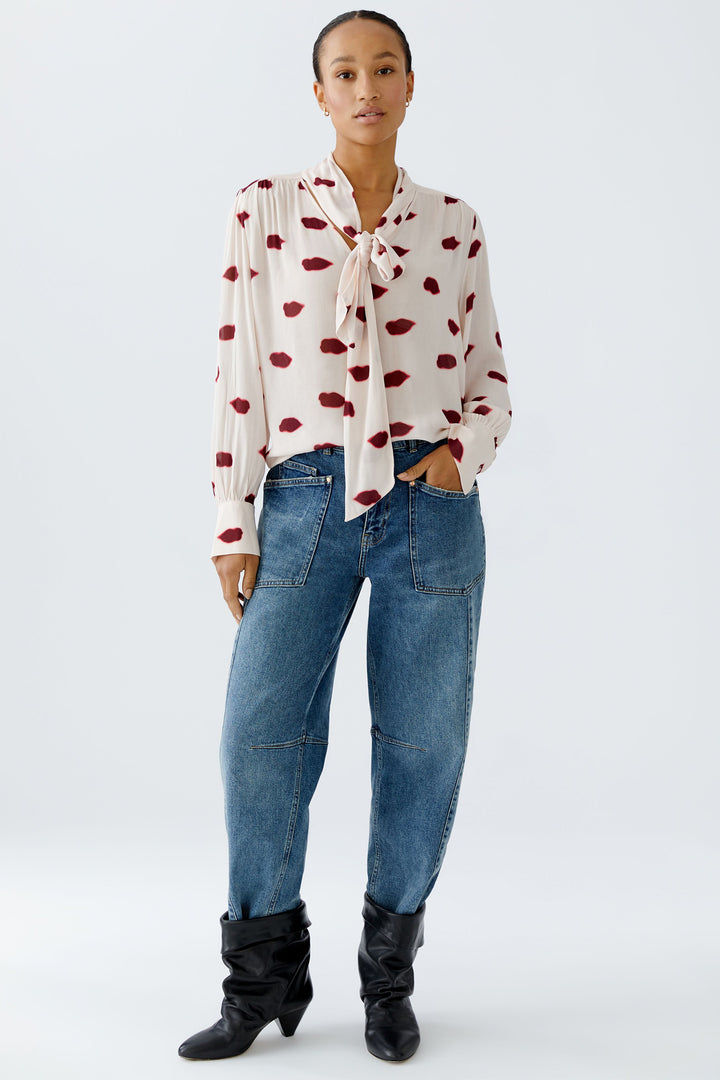 Woman wearing a white blouse with red patterns, blue jeans, and black boots on a white background