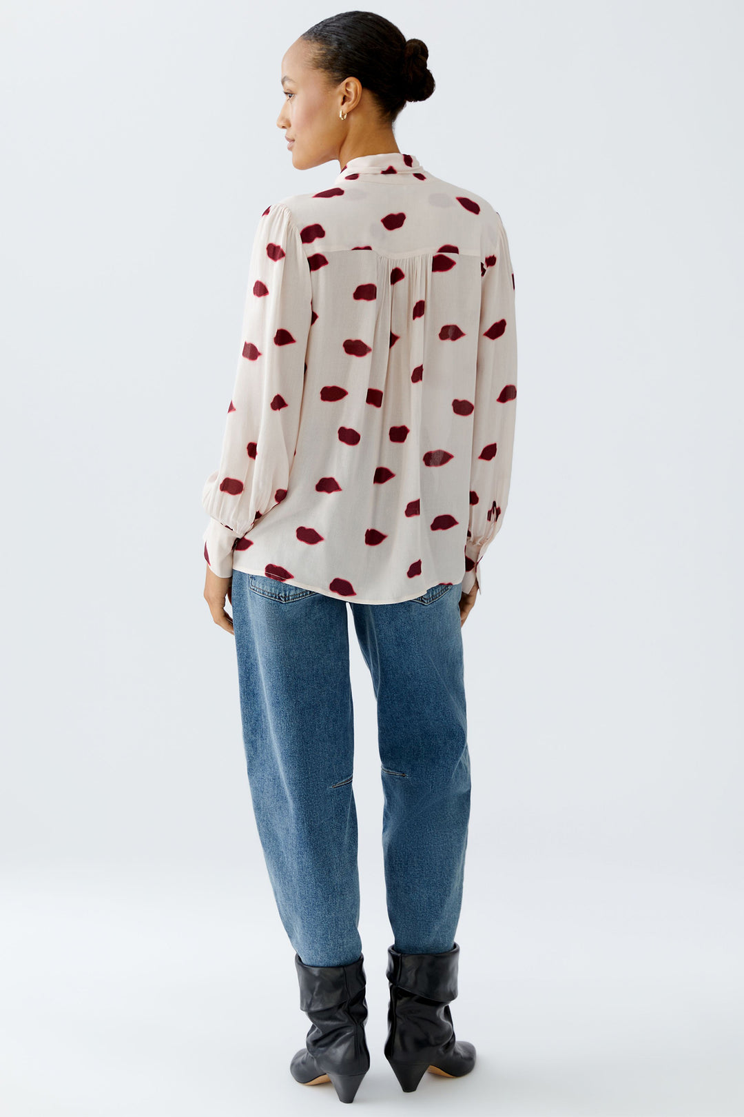 Person wearing a white blouse with red patterns and blue jeans on a white background