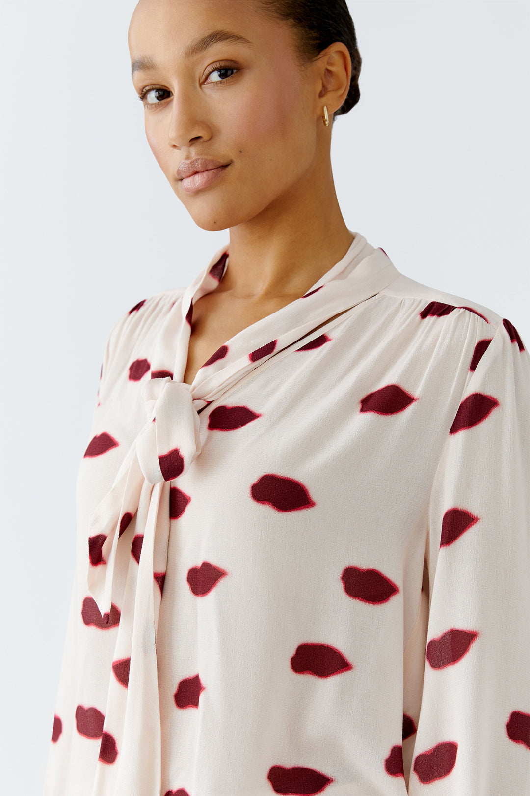 Woman wearing a cream blouse with red leaf patterns on a light gray background