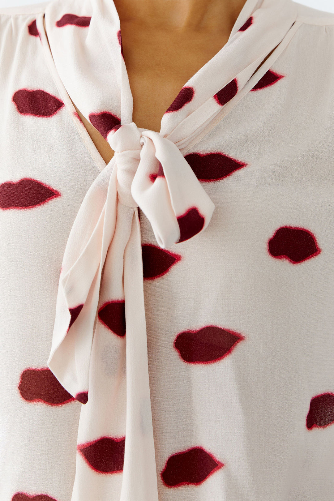 Close-up of a white blouse with red lip print and a knot detail.