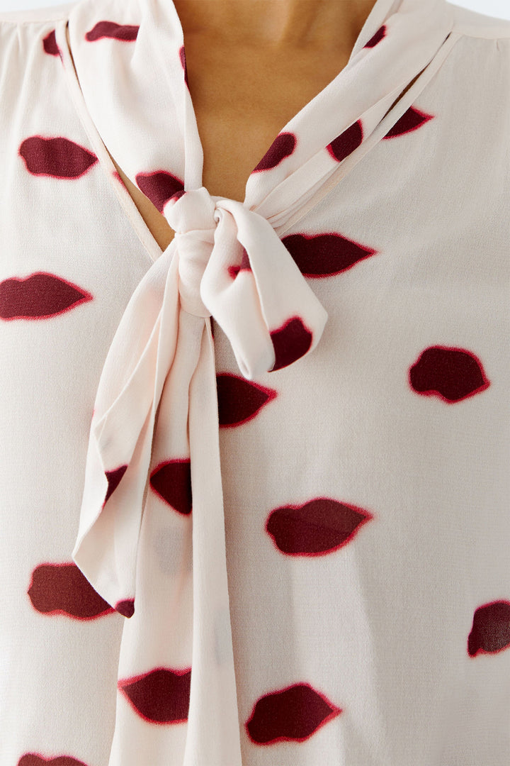 Close-up of a white blouse with red lip print and a knot detail.