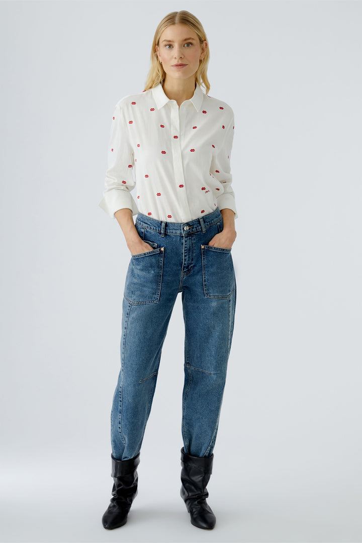 Woman wearing a white blouse with red polka dots and blue jeans on a white background