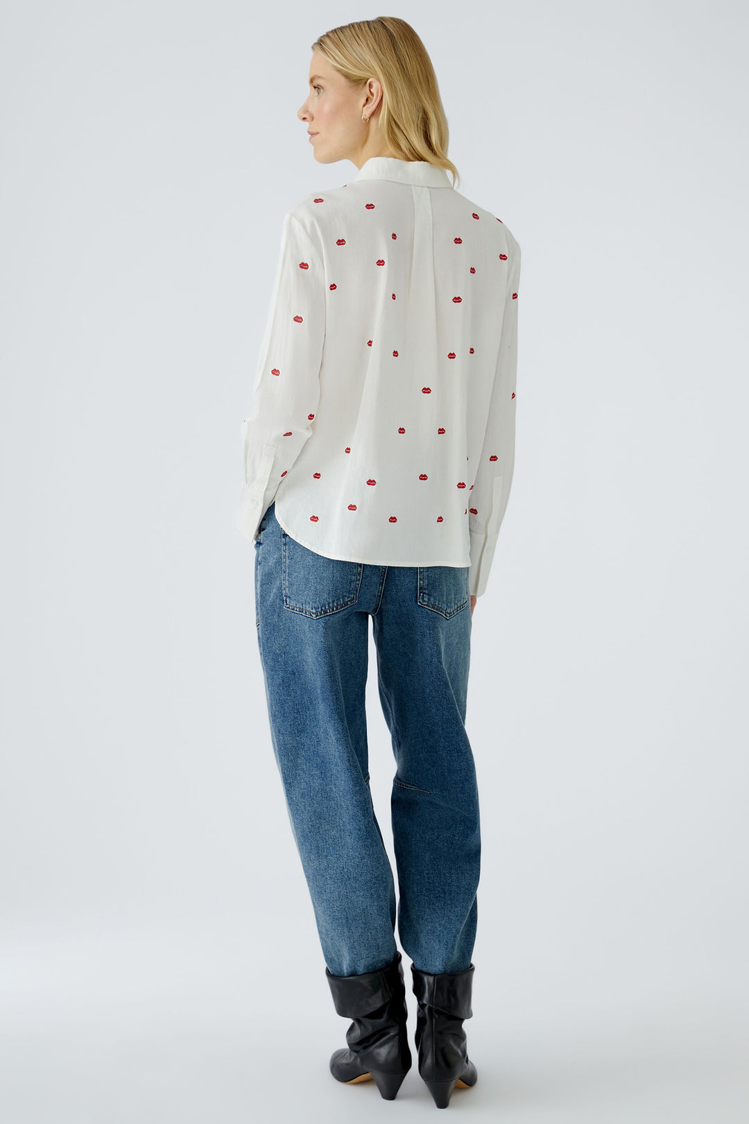 Person wearing a white blouse with red polka dots and blue jeans on a white background