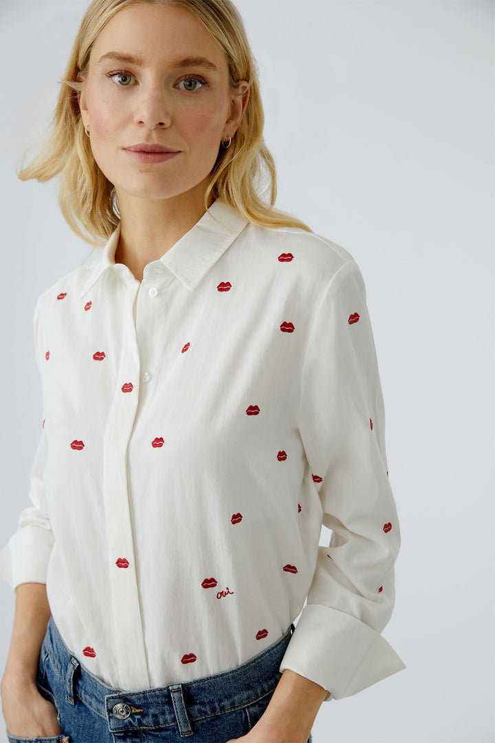 Woman wearing a white blouse with red pattern against a plain background