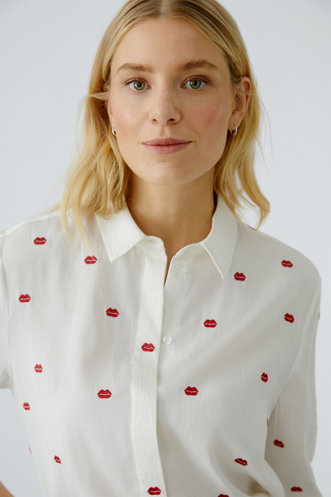 Woman wearing a white blouse with red lip print details on a plain background
