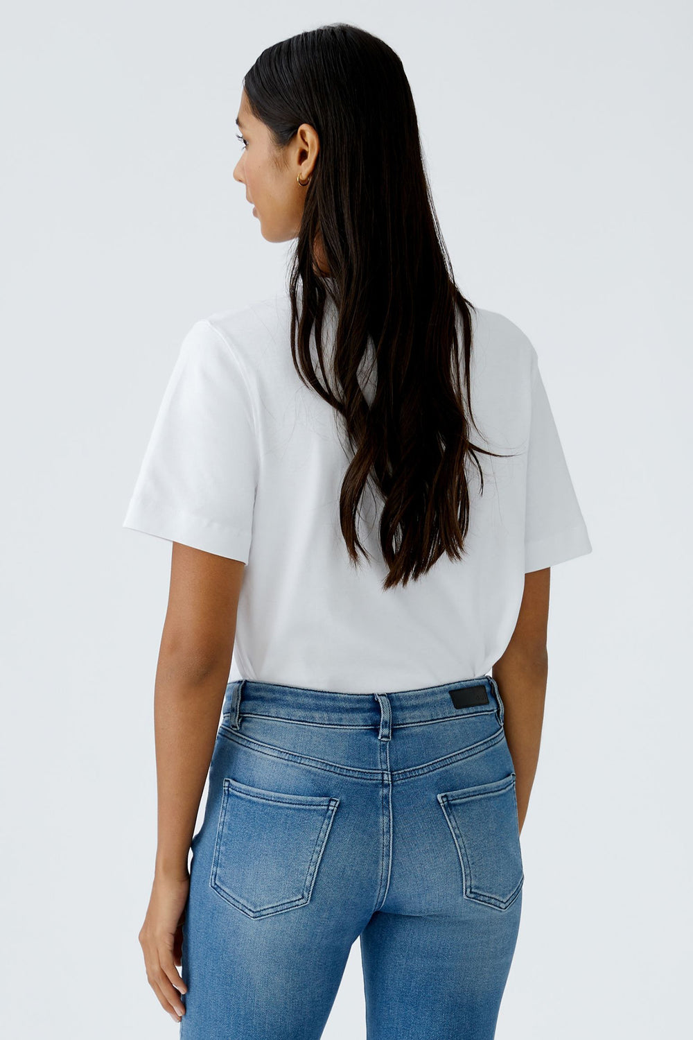 Person wearing a white t-shirt and blue jeans on a plain background