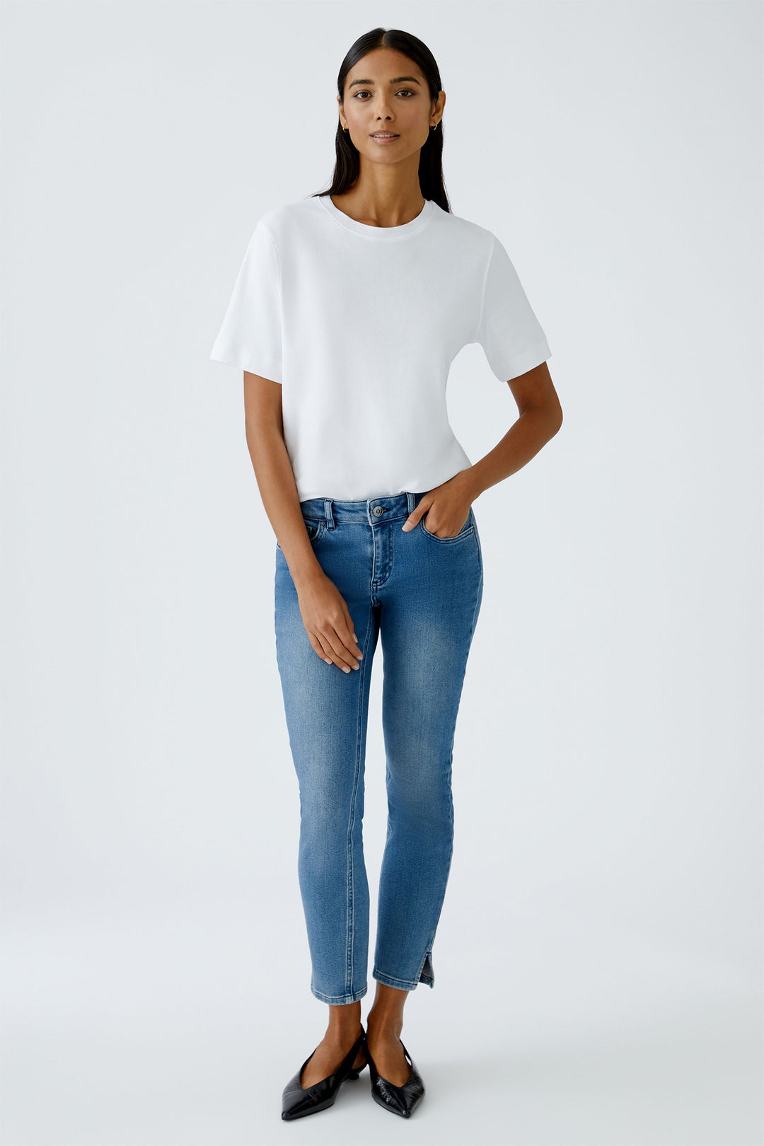 Woman wearing a white top and blue jeans on a plain background
