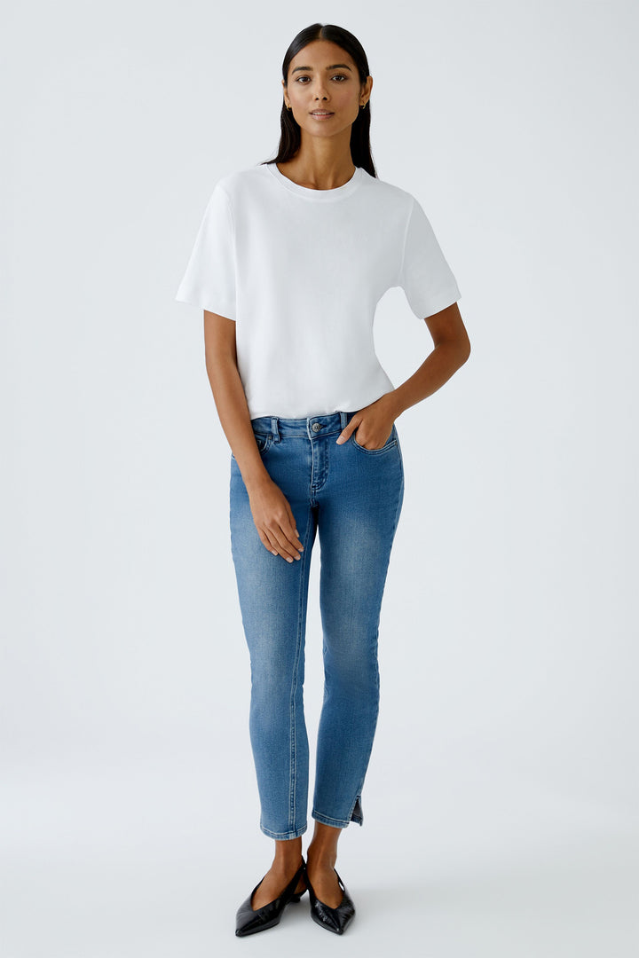 Woman wearing a white top and blue jeans on a plain background