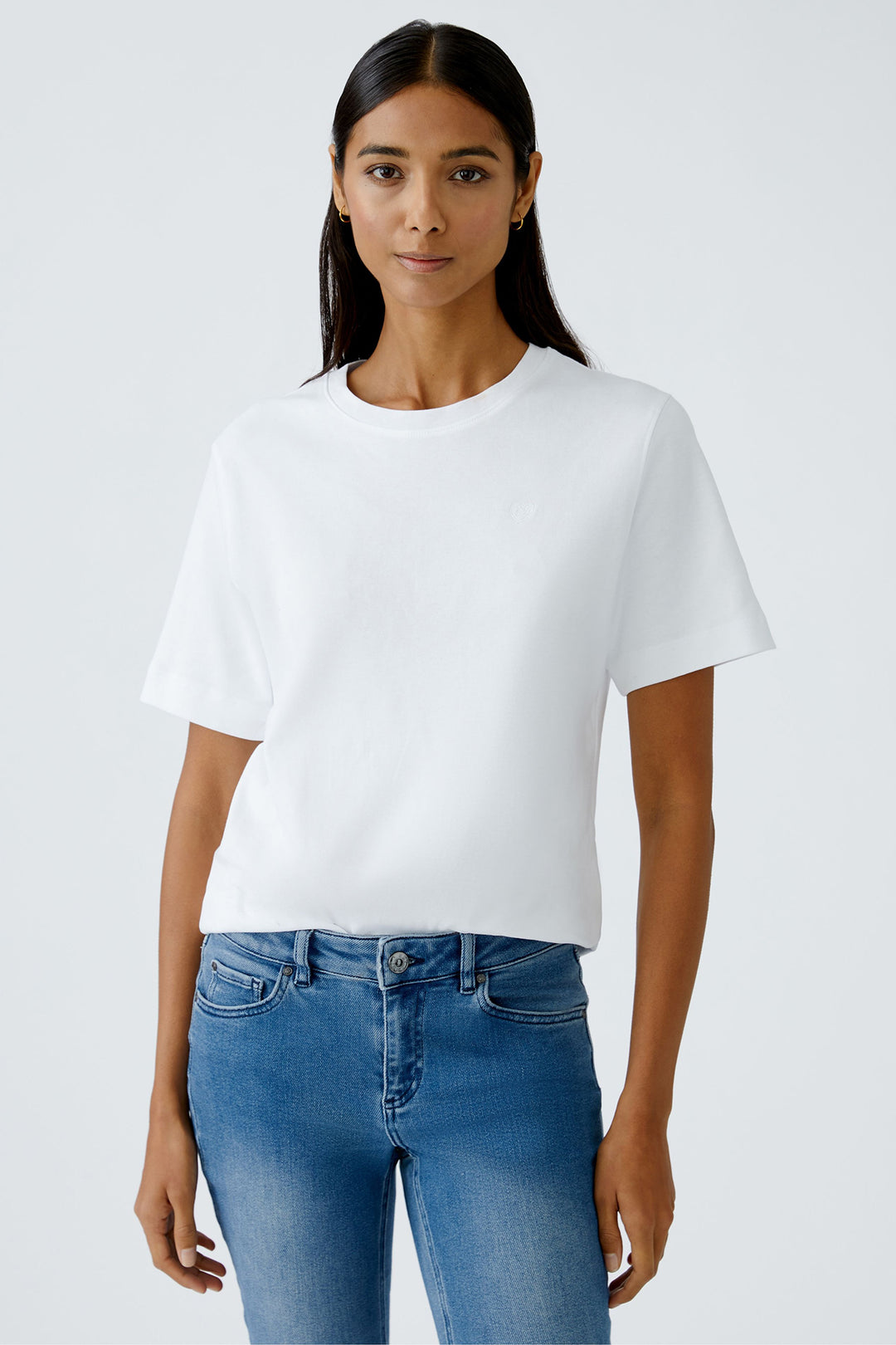 Woman wearing a white t-shirt and blue jeans against a plain background