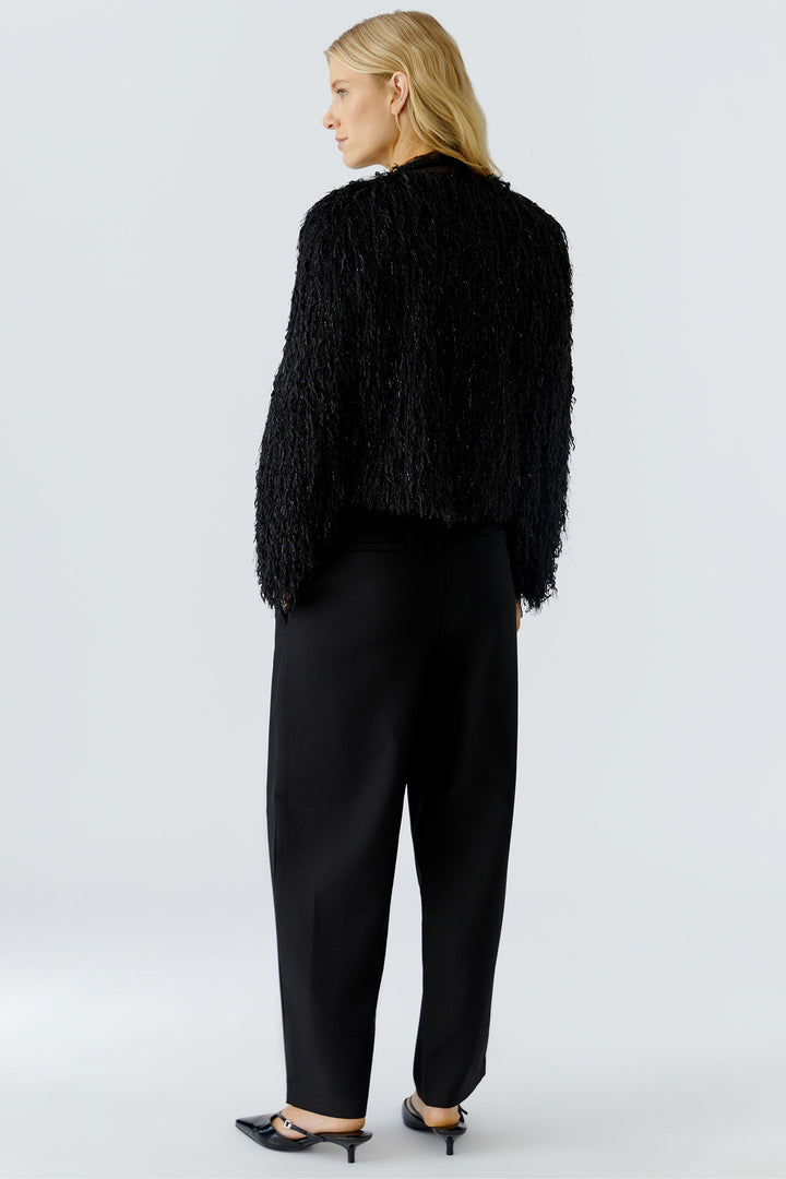 Person wearing a black textured cardigan and black pants on a light gray background