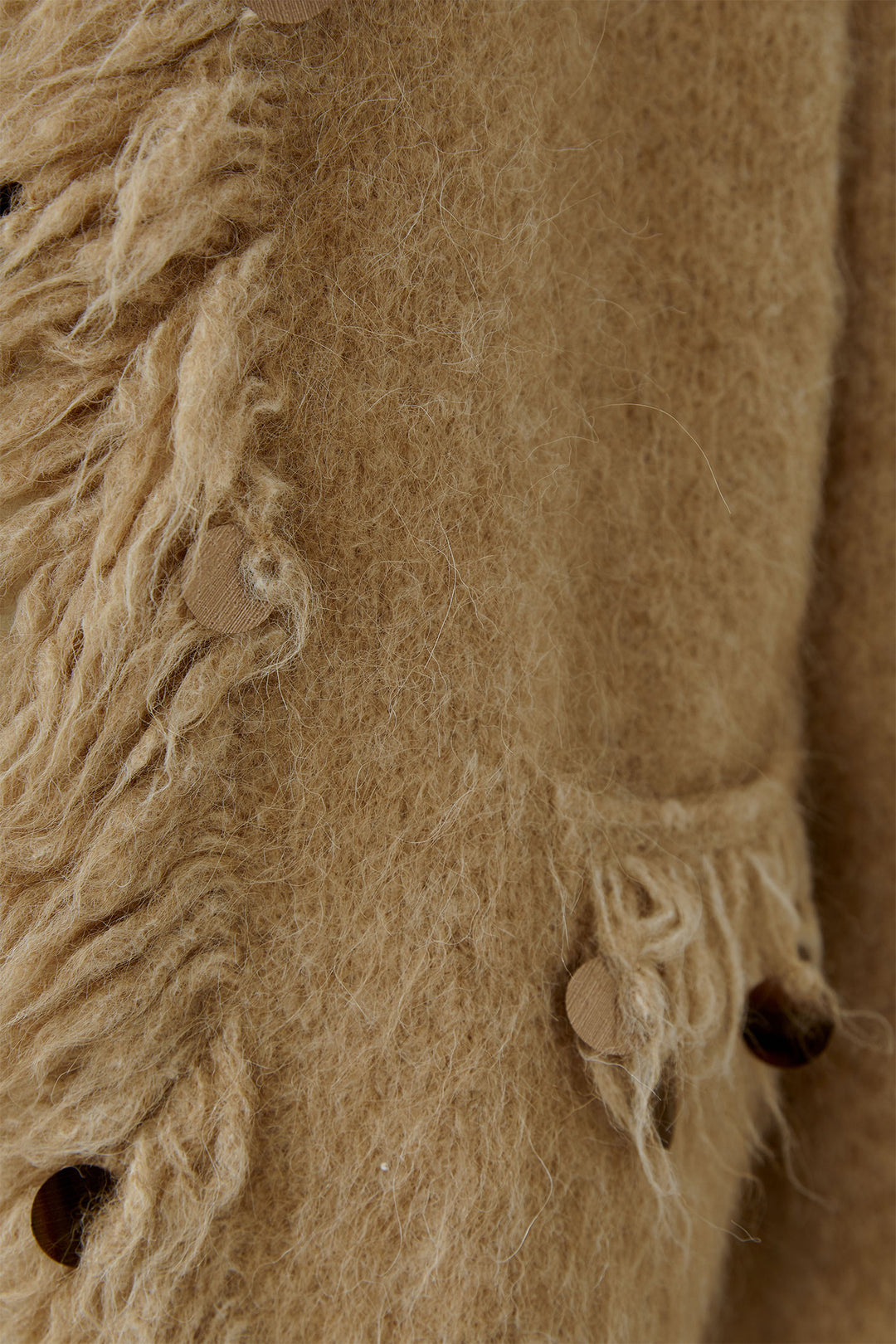 Close-up of a textured beige fabric with fringes and buttons.