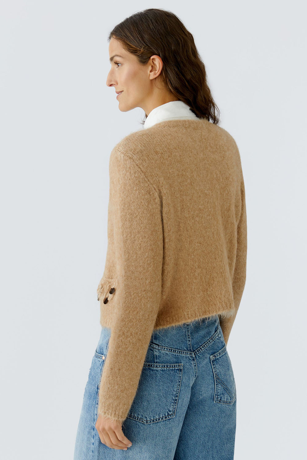 Woman wearing a beige sweater and blue jeans on a light gray background