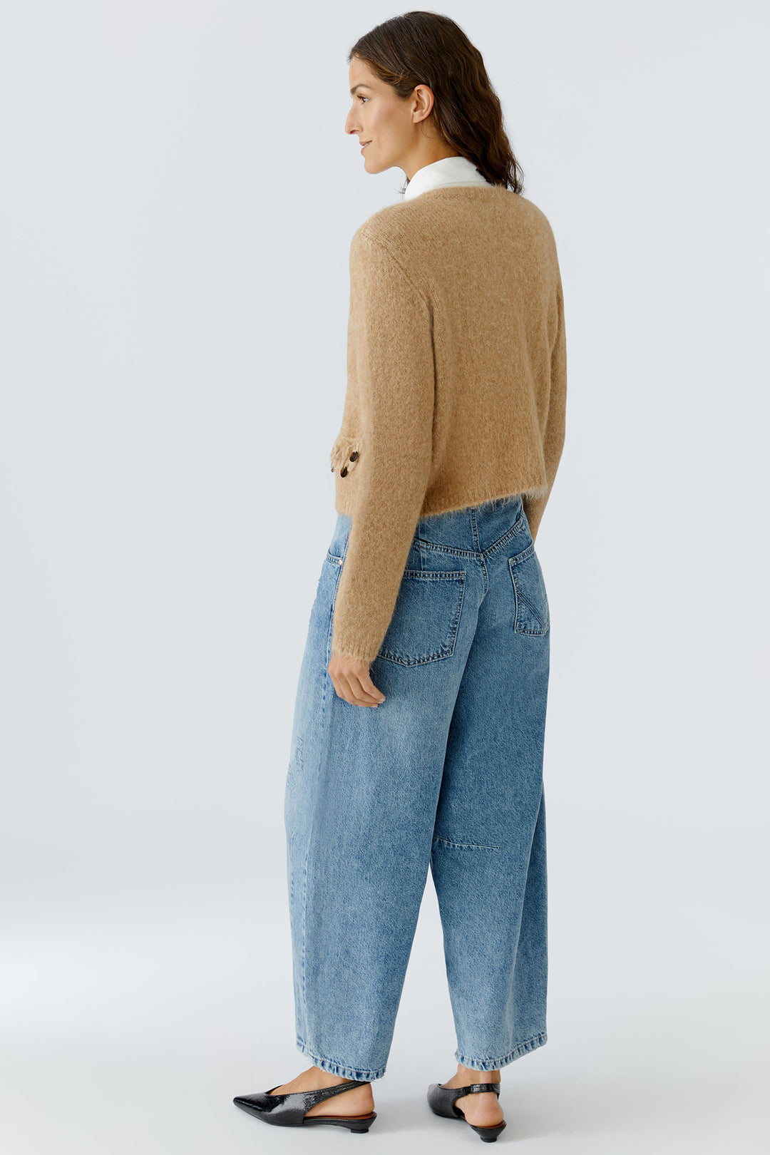Woman wearing a beige sweater and blue jeans on a white background