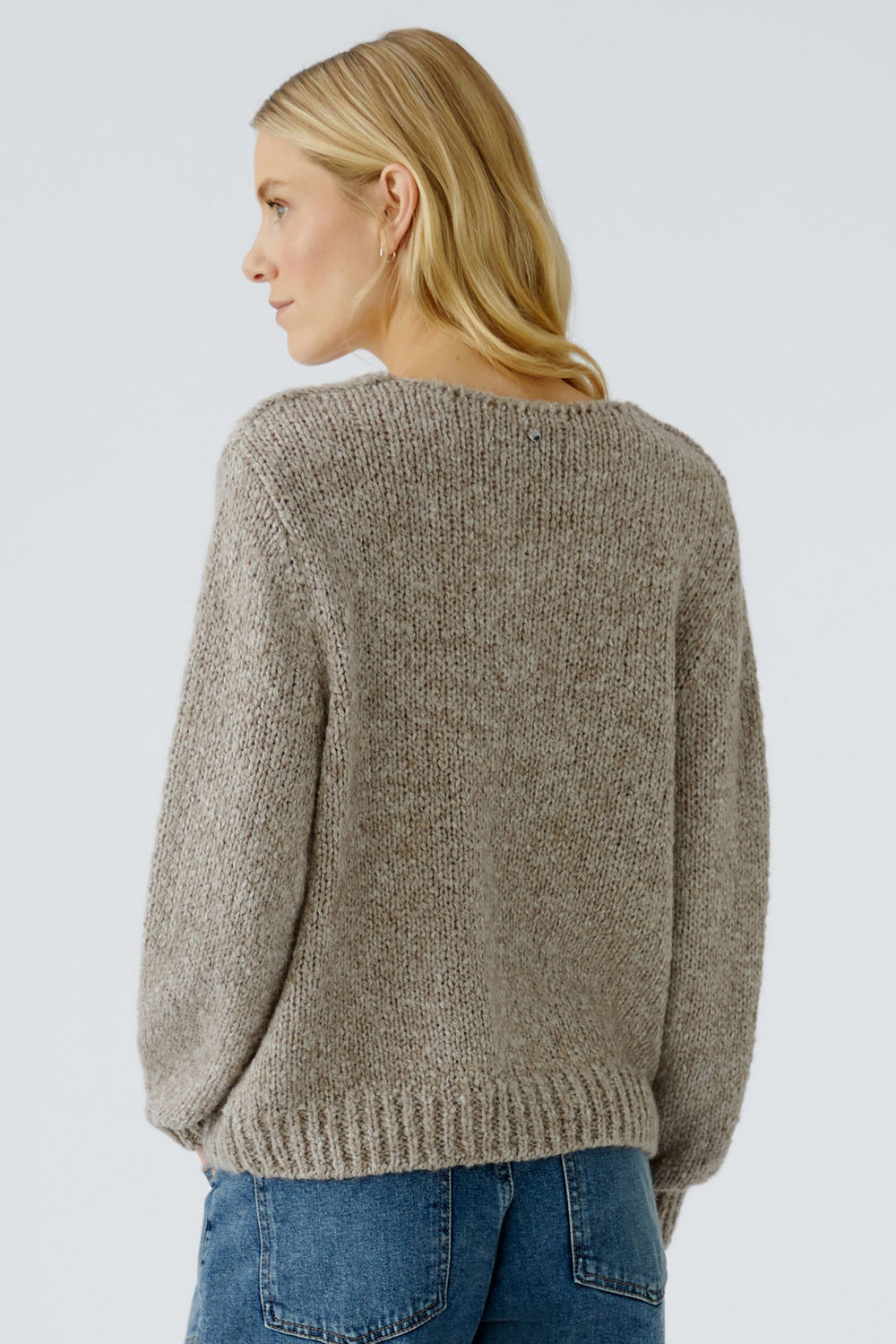 Woman wearing a beige sweater and blue jeans on a light gray background