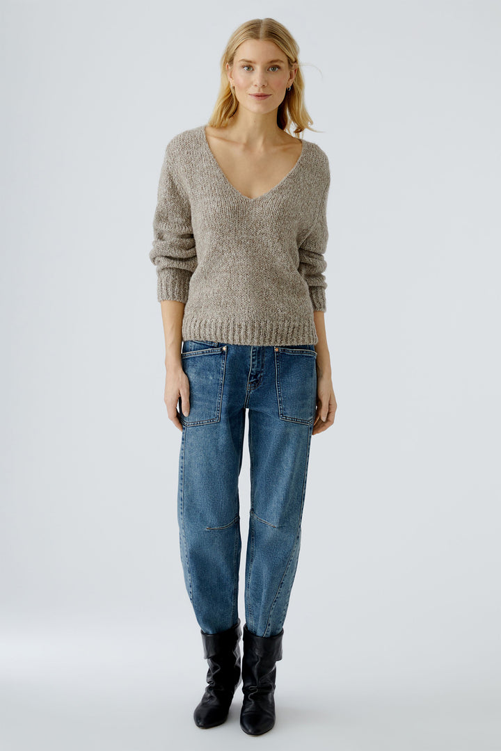 Woman wearing a gray sweater, blue jeans, and black boots on a white background