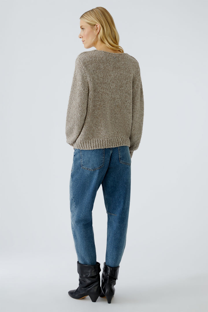 Person wearing a beige sweater, blue jeans, and black boots on a white background