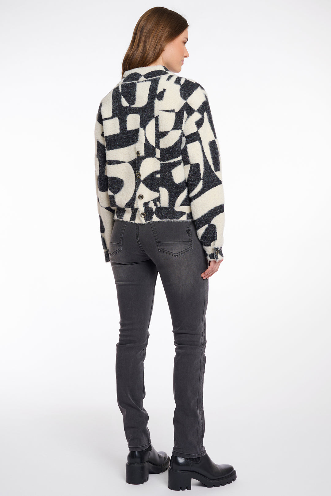 Woman wearing a patterned jacket and gray jeans on a white background